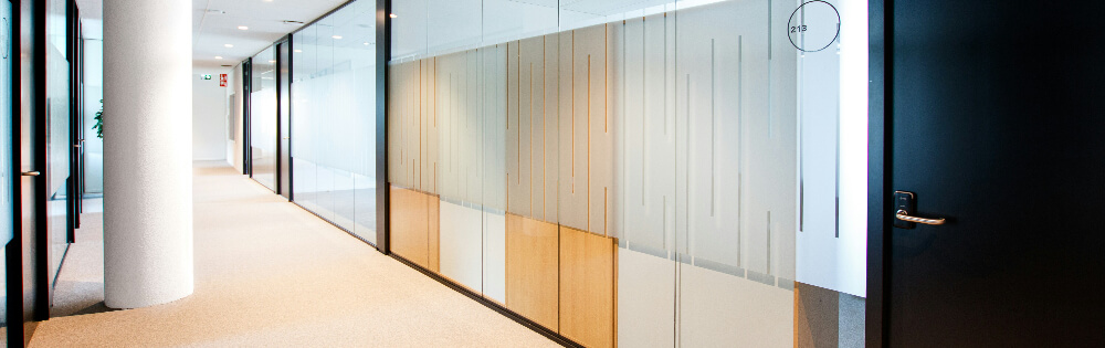 Inhaltsversicherung Moderner Büroflur mit Glaswänden, Holztüren und heller Beleuchtung.